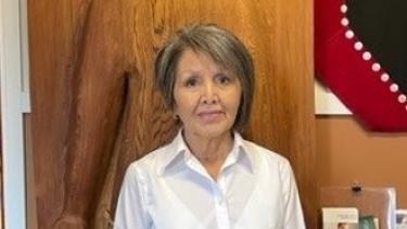 Female First Nations Elder wearing white button down shirt and blue jeans poses for photo