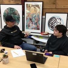One adult male and one youth male sitting at a desk and talking