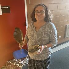 Female Elder stands holding a feather, prepared for smudging
