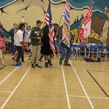 People gathered for the beginning of the powwow, three flags are being held up