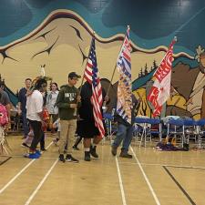 People gathered for the beginning of the powwow, three flags are being held up