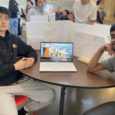 Two male students sitting at table with laptop displaying their project