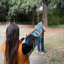 Two females each holding an end to an Indigenous patterned blanket as they fold it for the honouring.